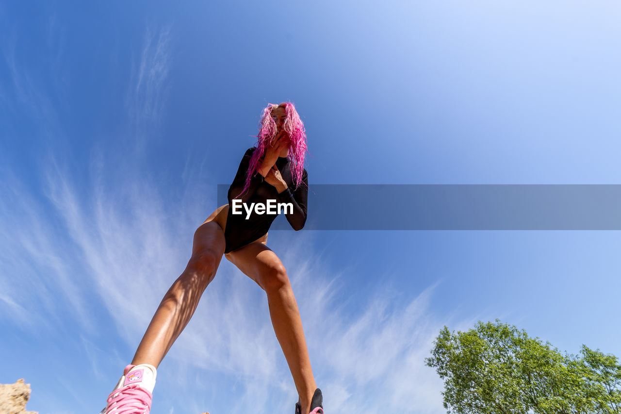 low angle view of young woman jumping against blue sky