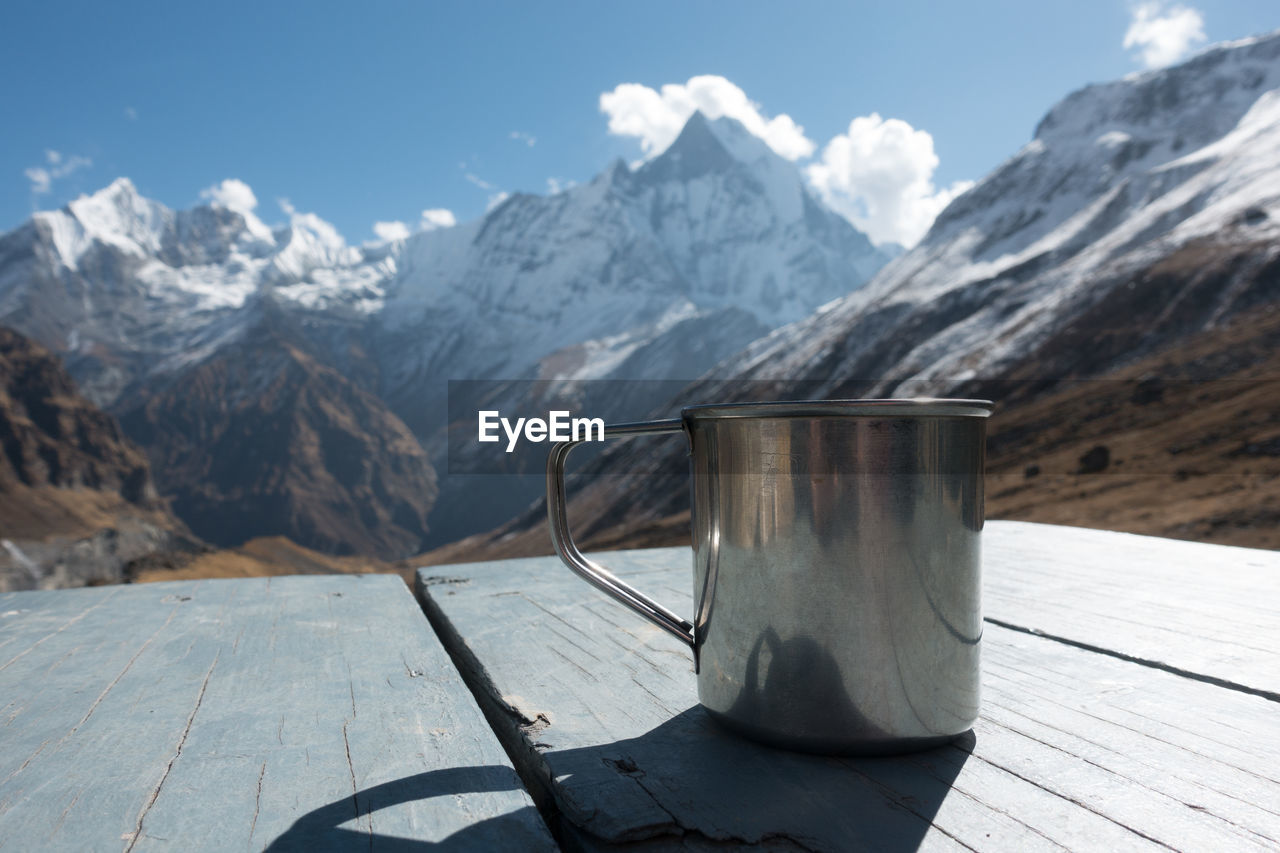 Close-up of mug on table against snowcapped mountains