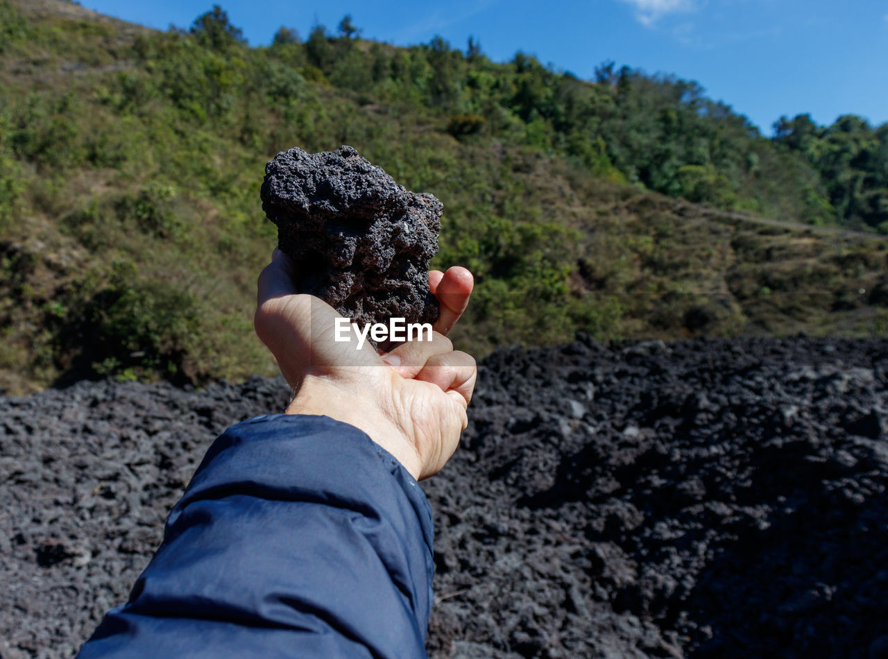 Man holding volcanic black porous stone or rock on active pacaya with recently dried black lava