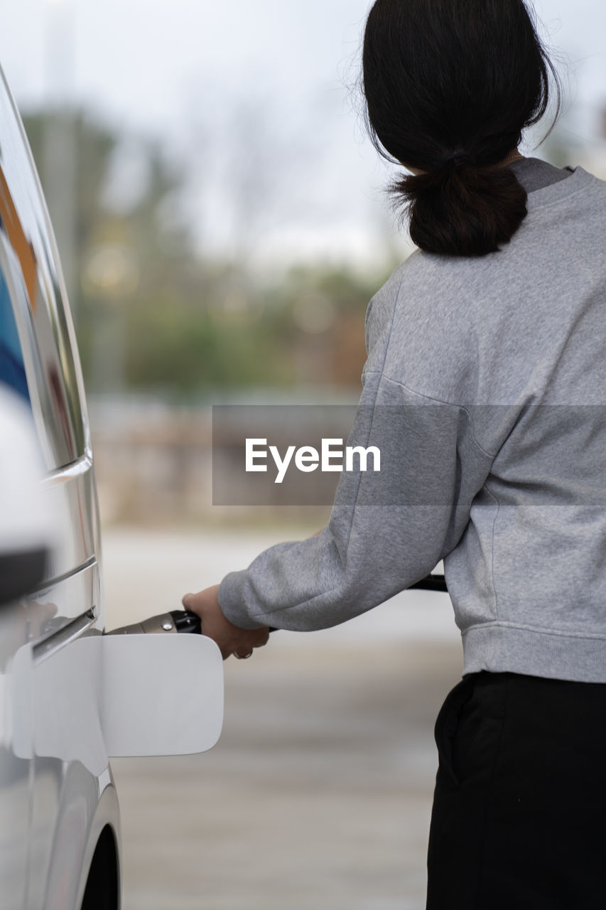 Rear view of woman in sport clothes refuelling the car