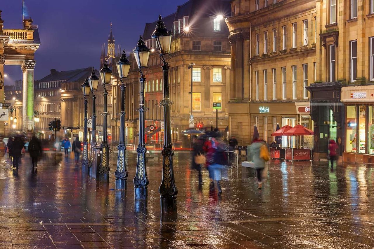 People walking on wet street in city at night during rainy season