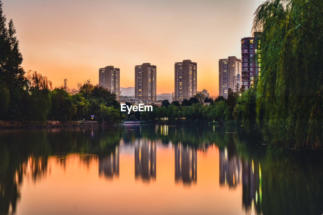 Reflection of trees and buildings in lake during sunset