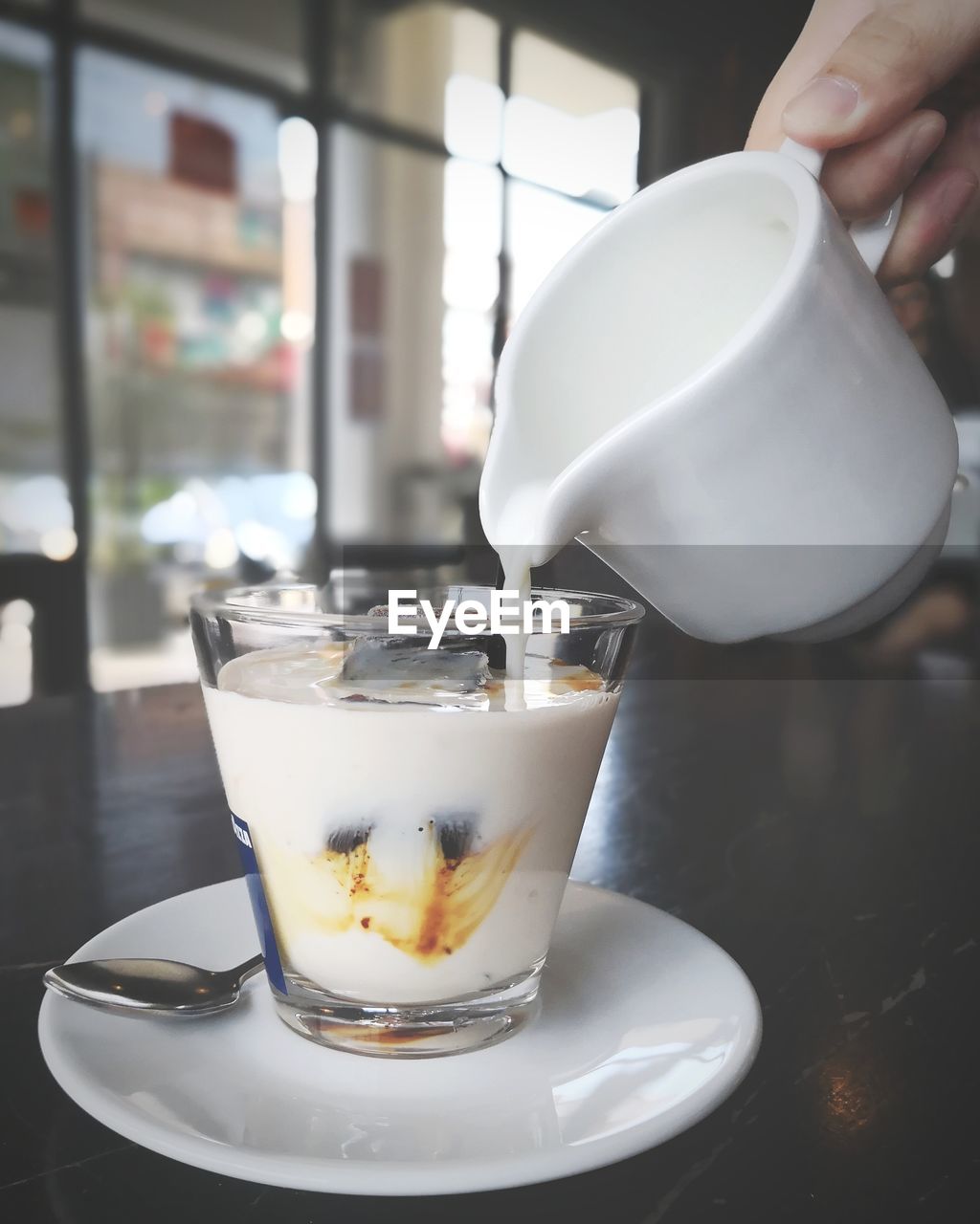 Close-up of hand pouring milk in coffee cup on table