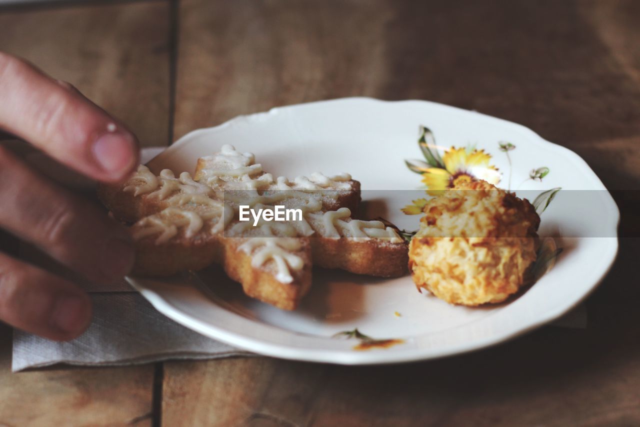 Cropped hand holding gingerbread cookie in plate on table