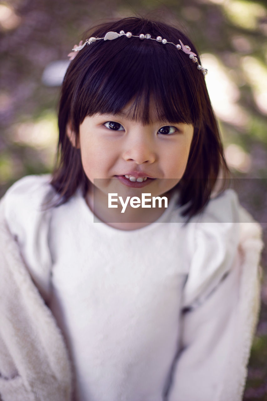 Korean girl in a white light fur coat and a headband stands in a garden with cherry blossoms