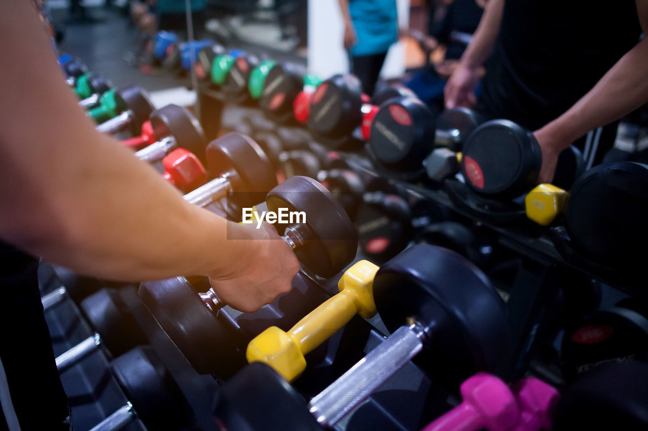 Cropped hand of men lifting dumbbell in gym