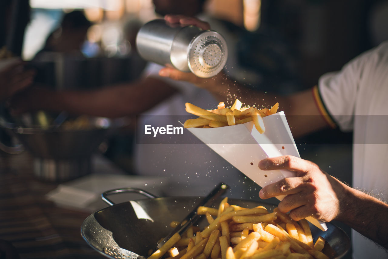 Midsection of man dusting salt on french fries