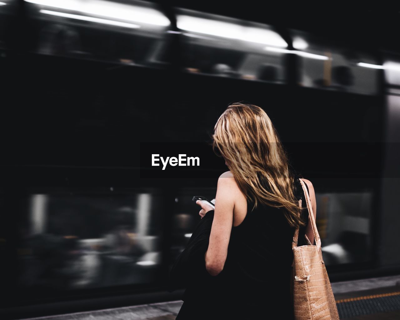 Rear view of woman using mobile phone at railroad station platform