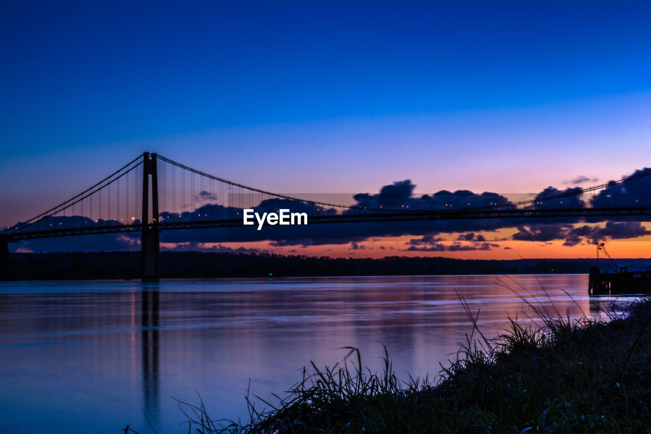 Silhouette tancarville bridge over river against sky during sunset