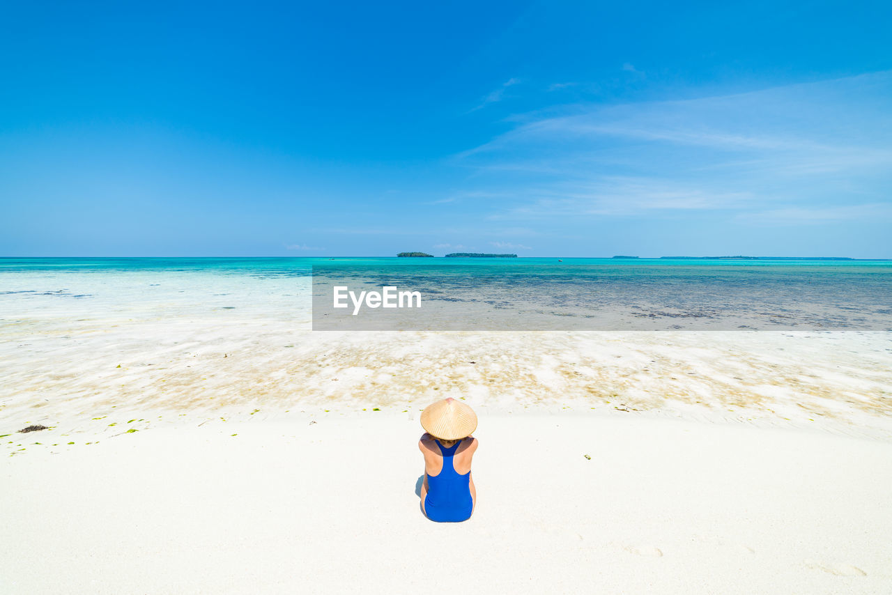 Rear view of woman sitting at beach against sky