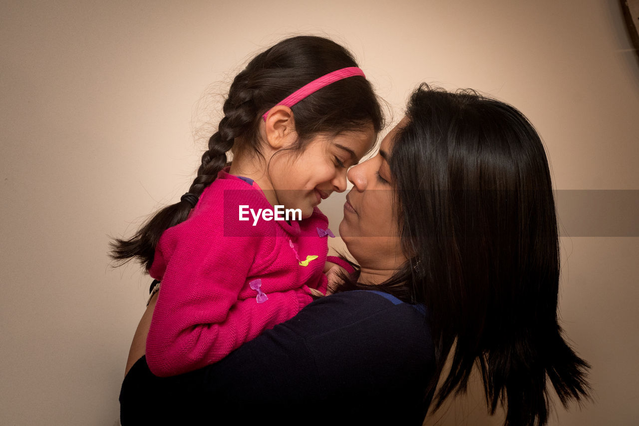 Happy mother carrying daughter against beige background