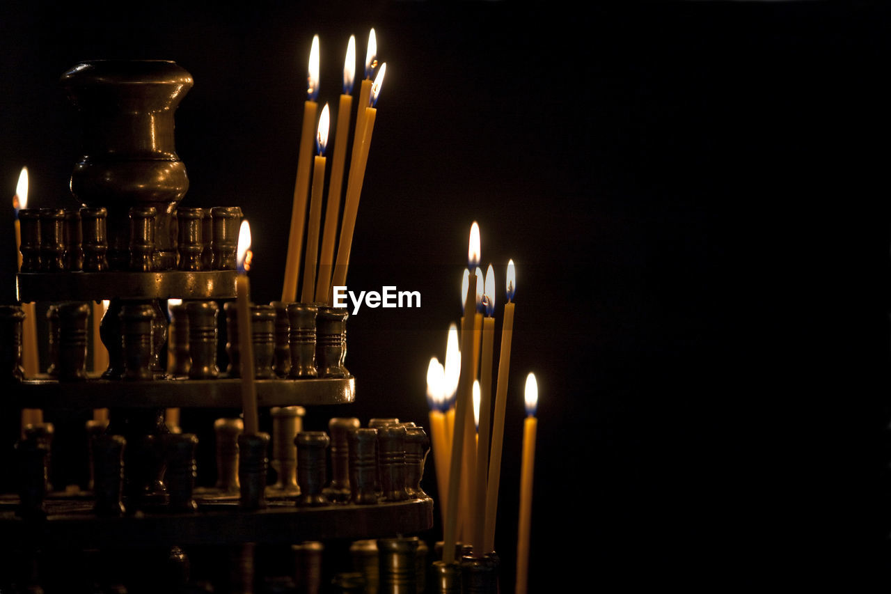 Close-up of lit candles in stand against black background
