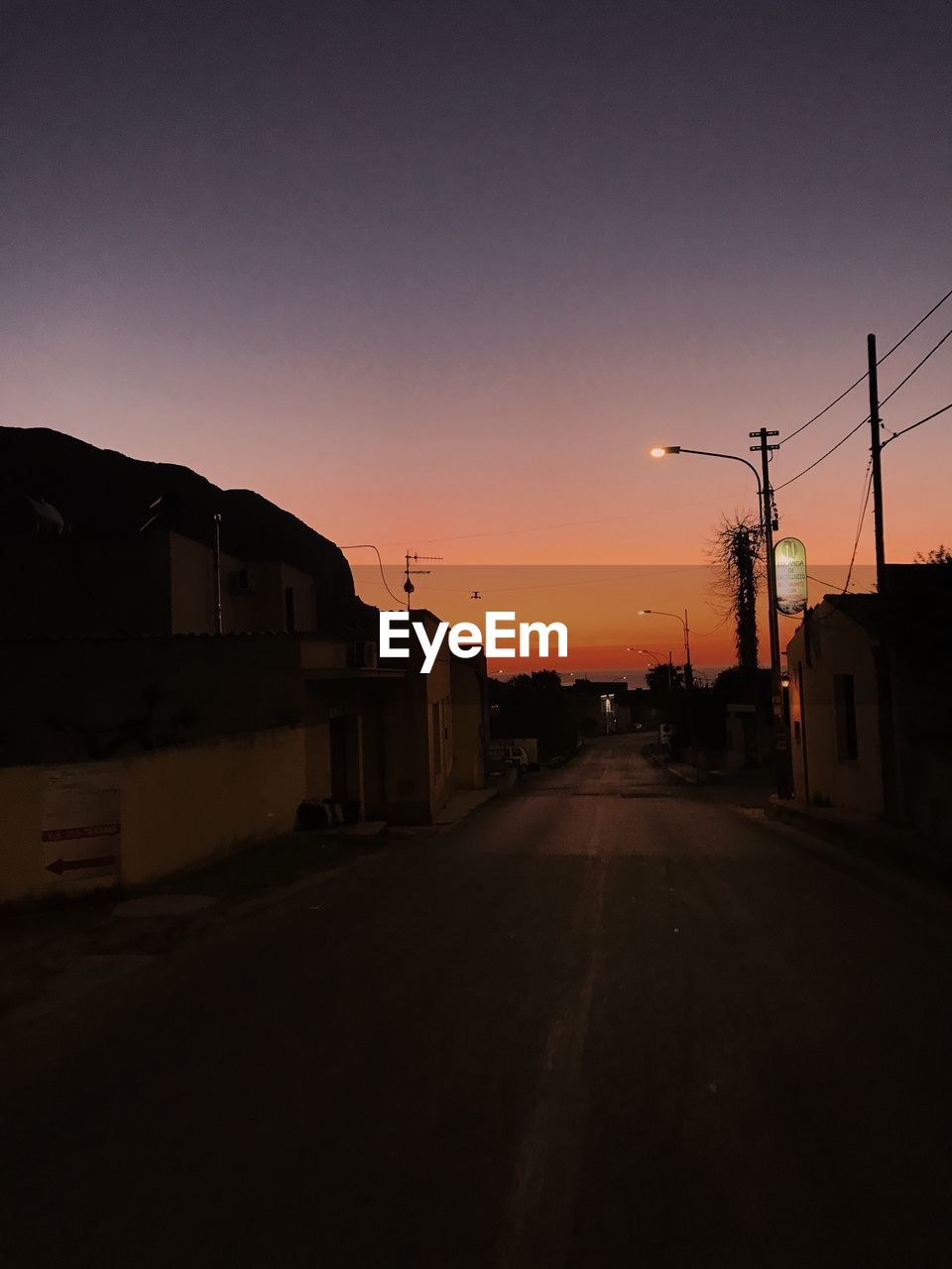 STREET BY BUILDINGS AGAINST SKY DURING SUNSET