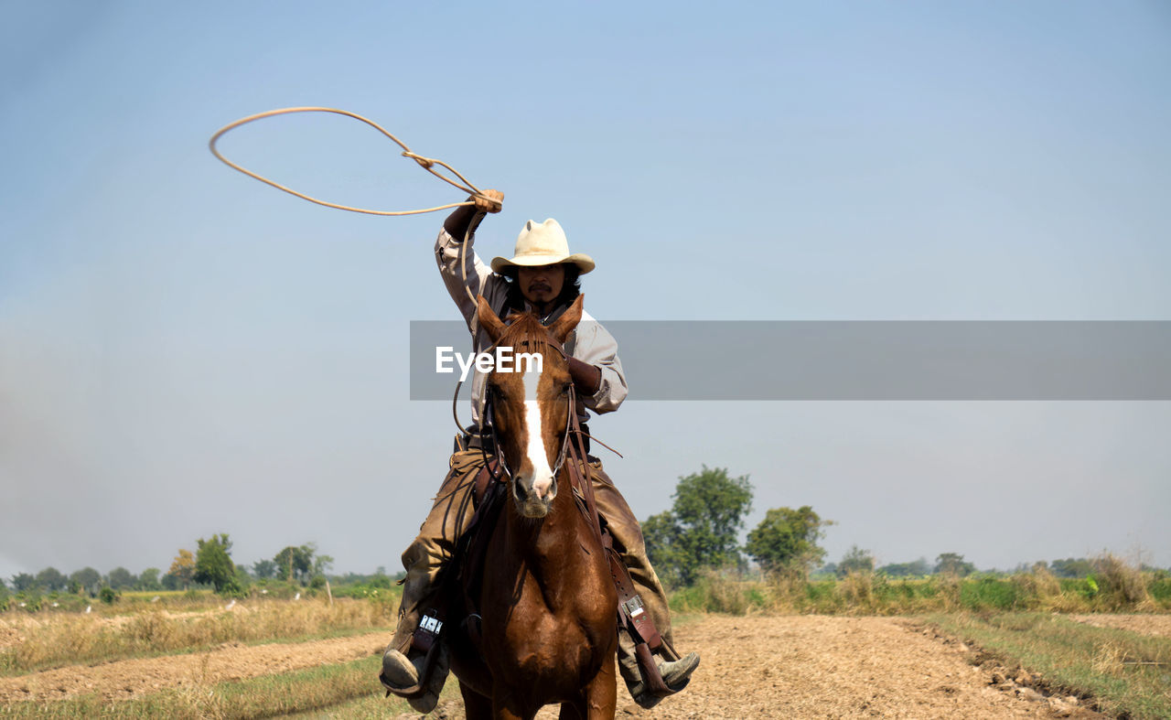 Man holding noose while riding on horse against sky