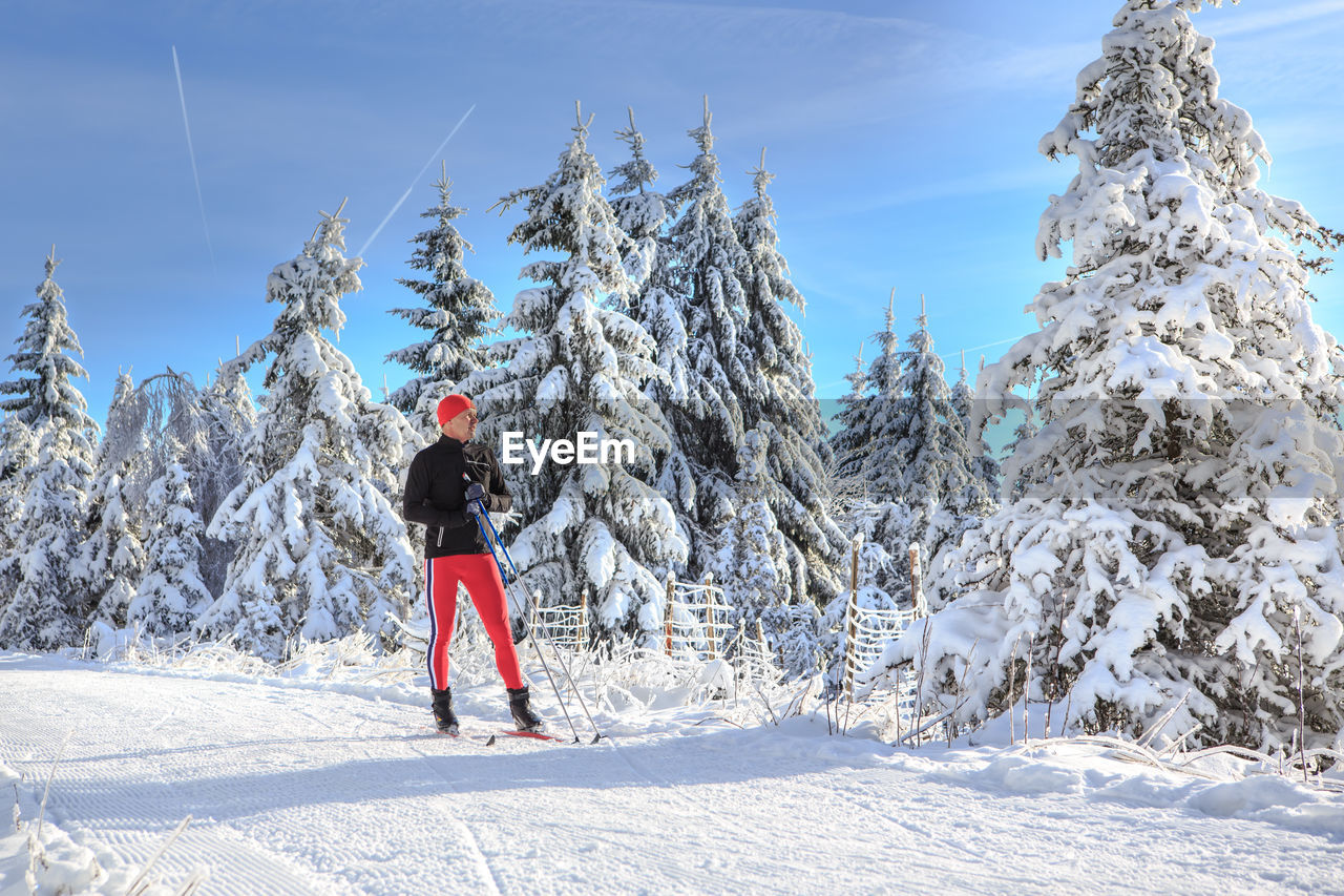 Man skiing on snow covered field against trees