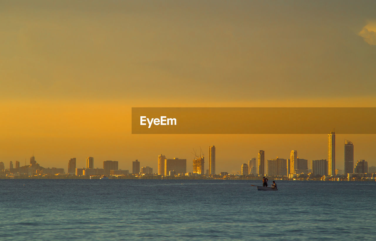 Sea by buildings against sky during sunset