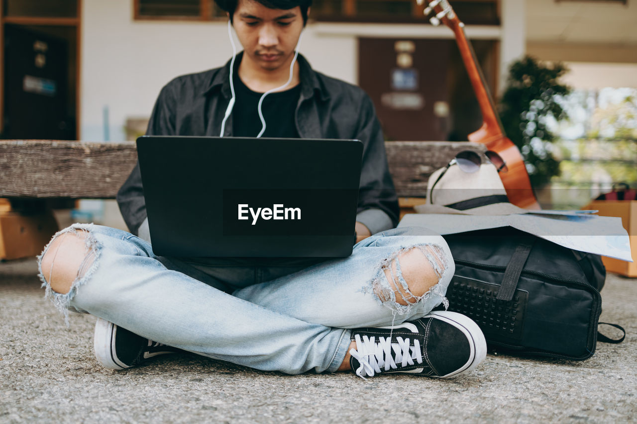 Low section of man using laptop while sitting outdoors