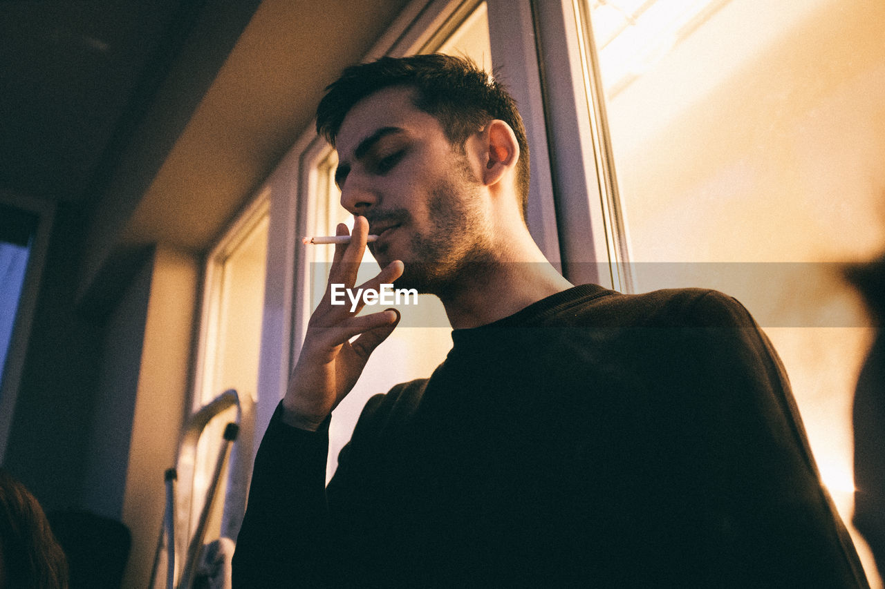 Man smoking cigarette by window at home