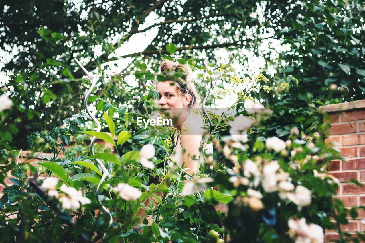 PORTRAIT OF SMILING YOUNG WOMAN WITH PLANTS