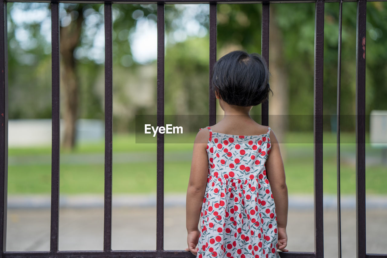 Adorable little girl standing behind the fence during coronavirus pandemic.