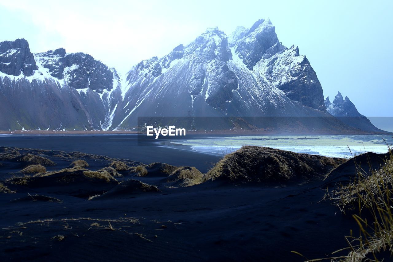 Scenic view of sea by snowcapped mountain against sky