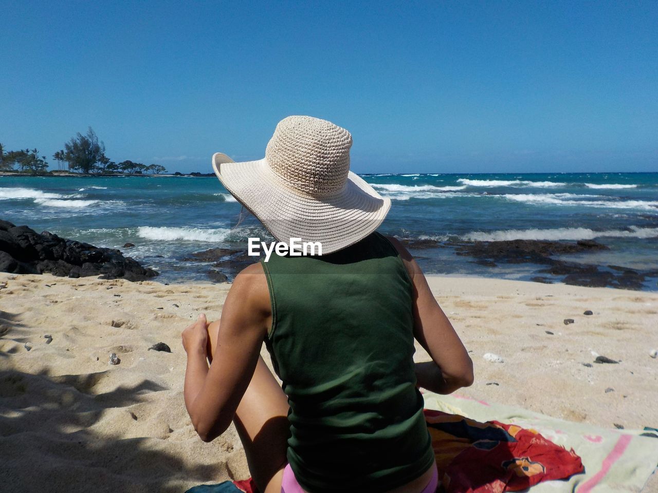 Rear view of woman sitting on beach against clear blue sky