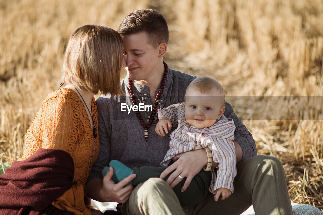 Couple with son kissing while sitting on land