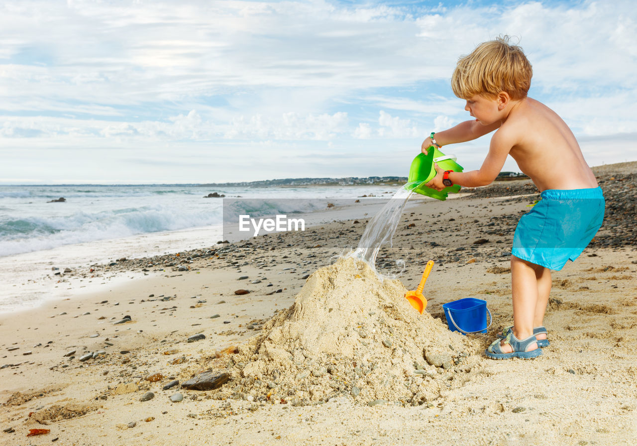 side view of boy playing with straw at beach against sky