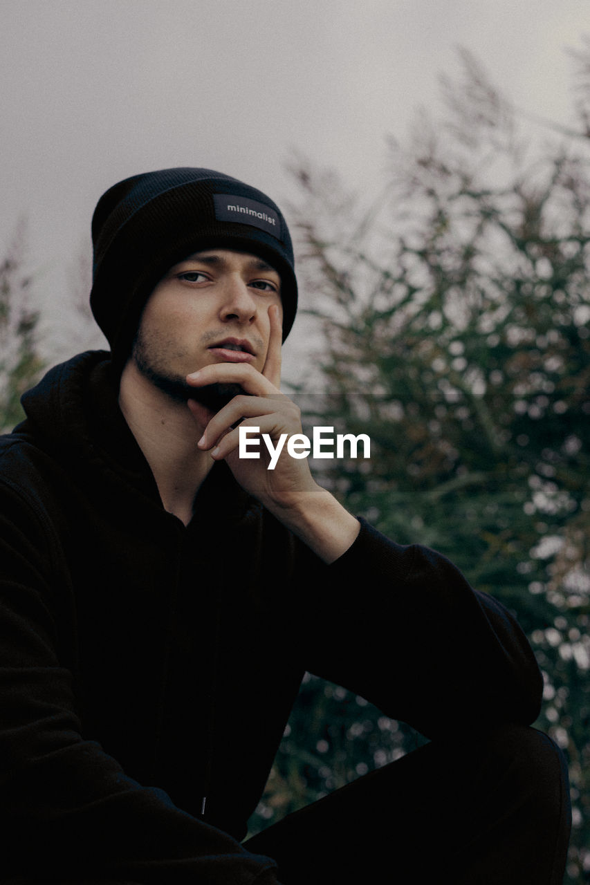 PORTRAIT OF YOUNG MAN LOOKING AWAY AGAINST PLANTS