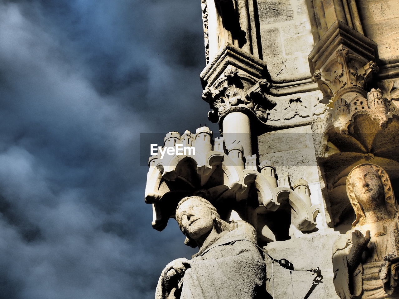 Statues on cropped wall against clouds