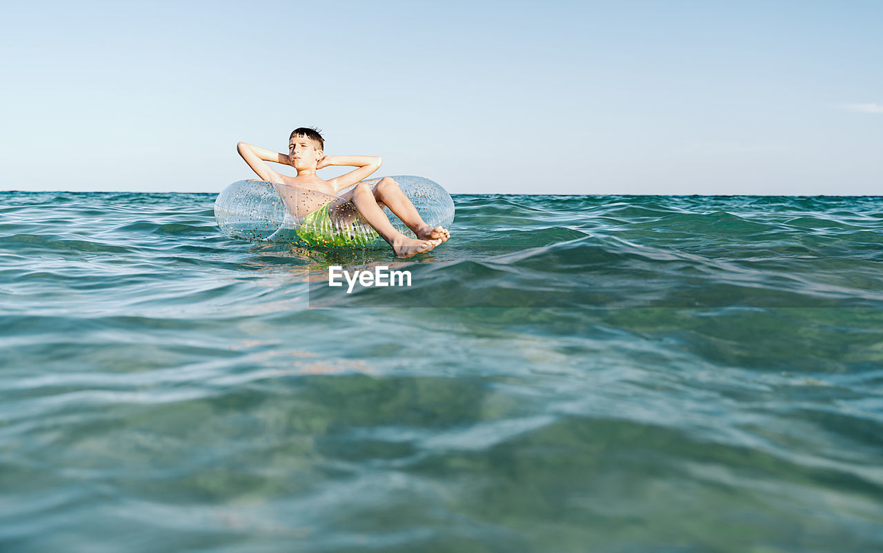 Relaxed white boy swimming in a float in the sea enjoying calm waves in summertime