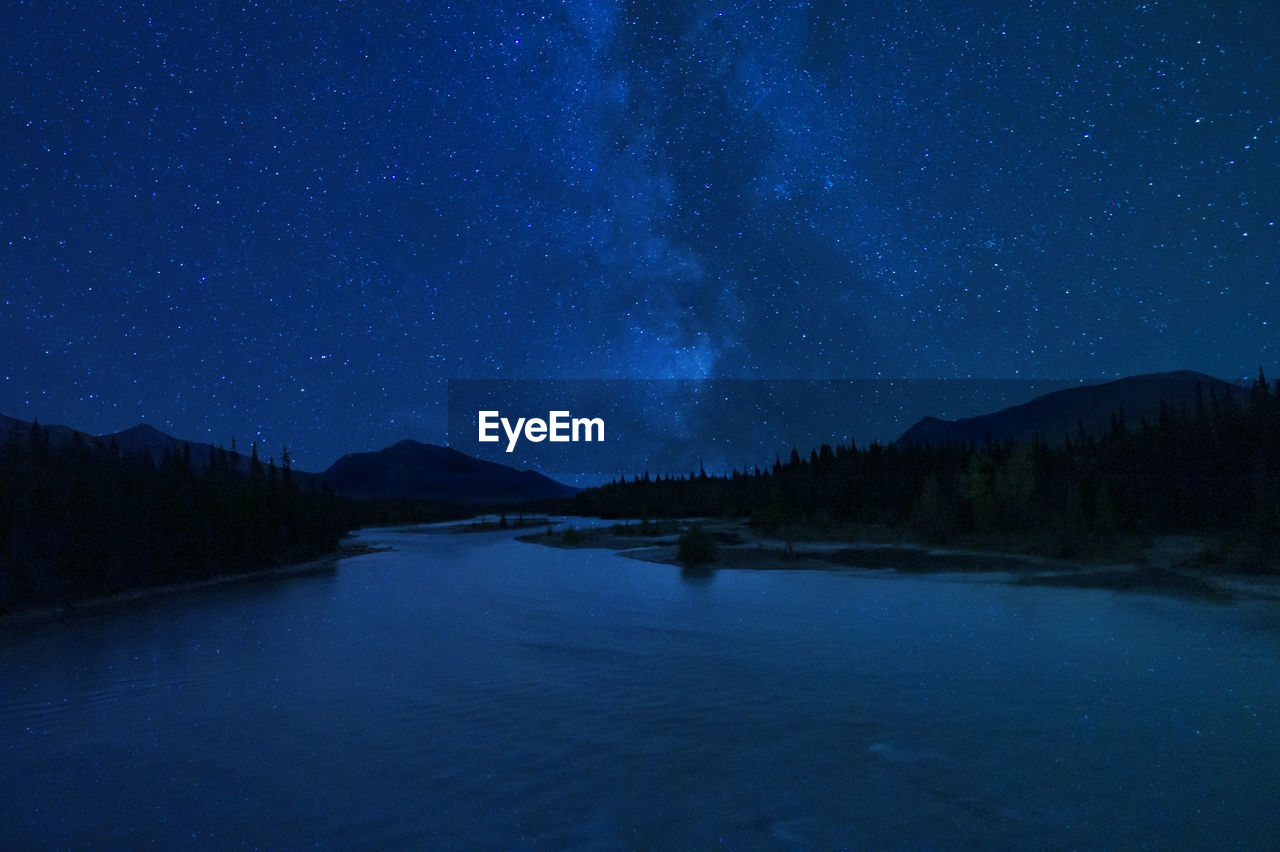 Stunning milky way night stars over mountain wilderness river pine trees