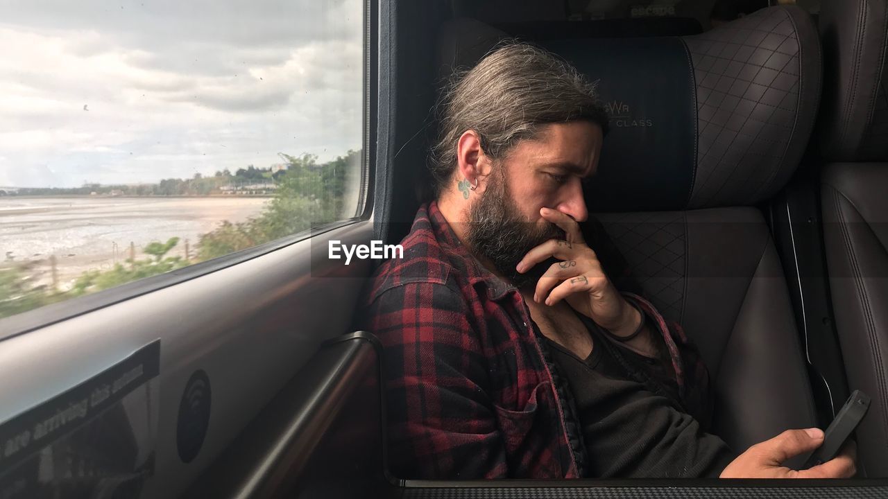 Thoughtful man using mobile phone while sitting in train