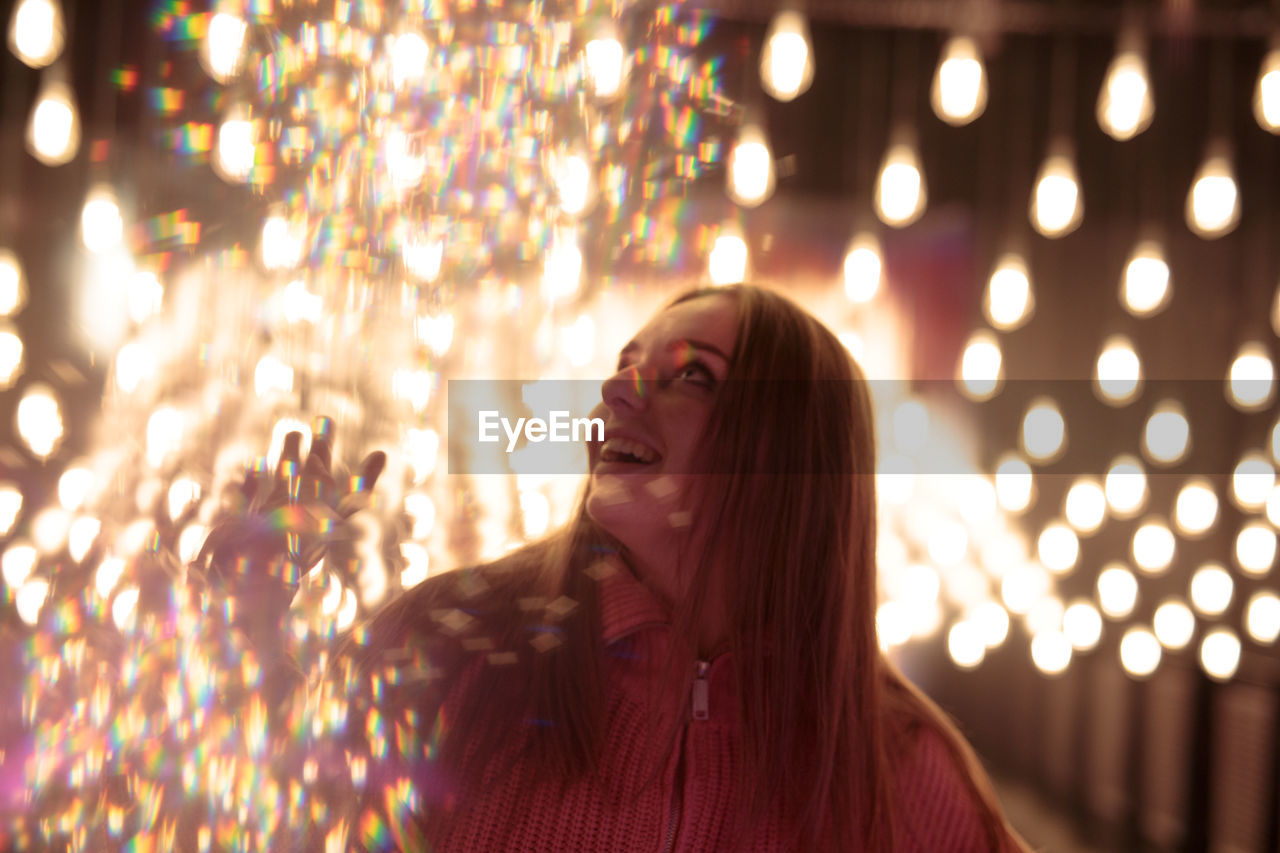 portrait of young woman standing against illuminated lights