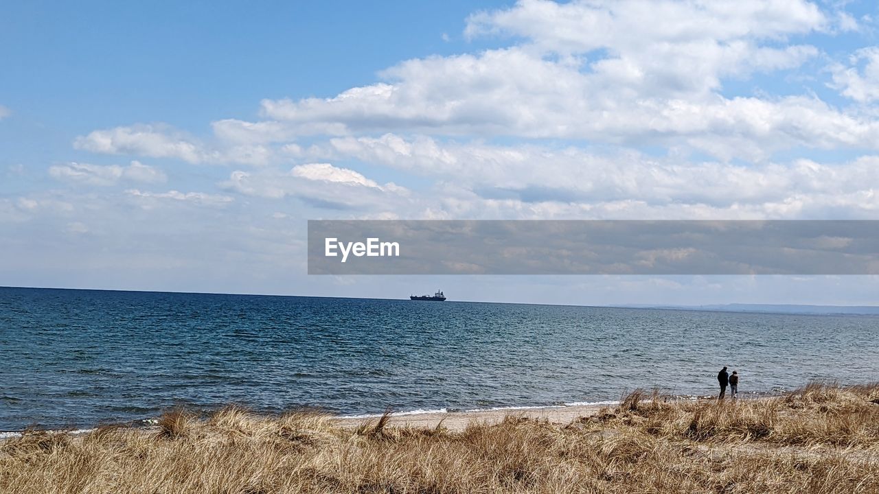 sky, water, sea, horizon, shore, beach, land, body of water, cloud, scenics - nature, beauty in nature, horizon over water, nature, ocean, coast, sand, tranquility, tranquil scene, day, holiday, vacation, trip, outdoors, leisure activity, non-urban scene, blue, bay, travel, idyllic, men, travel destinations, standing, one person, landscape, adult, wave, tourism, lifestyles, environment, rear view