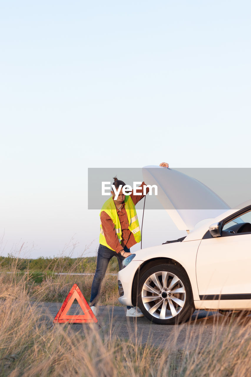 Overwhelmed young man with his car in need of repairment in the middle of nowhere in the countryside