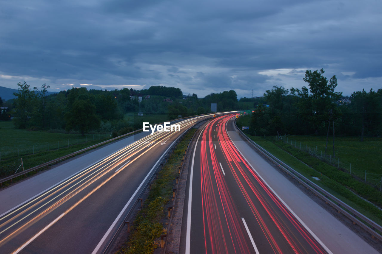 Light trails of vehicles on street against cloudy sky