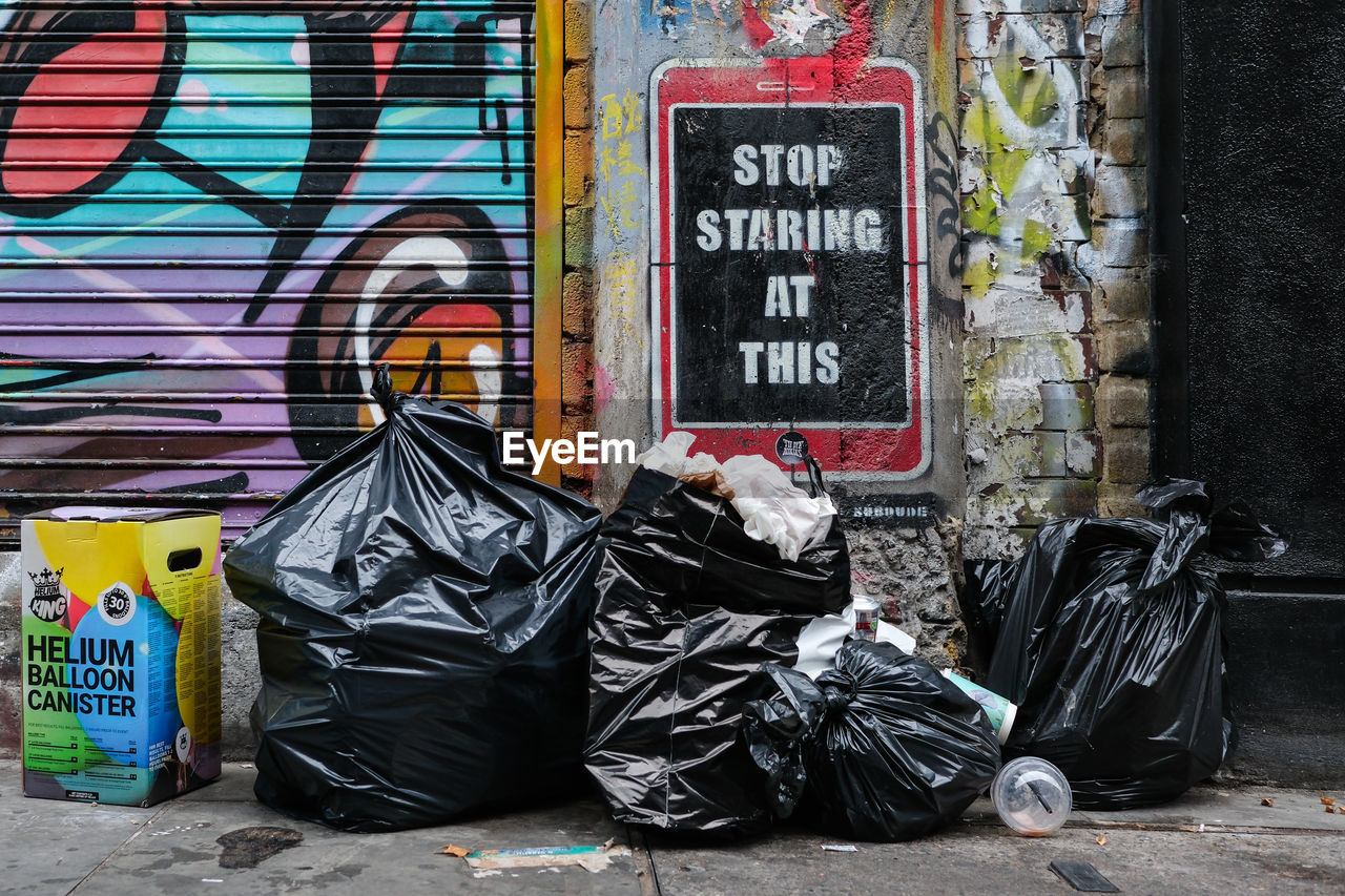 street, road, urban area, waste container, graffiti, text, art, communication, city, architecture, western script, wall - building feature, day, street art, infrastructure, built structure, painting, footpath, no people, social issues, handwriting, sign, sidewalk, building exterior, litter, outdoors, garbage, creativity, waste containment
