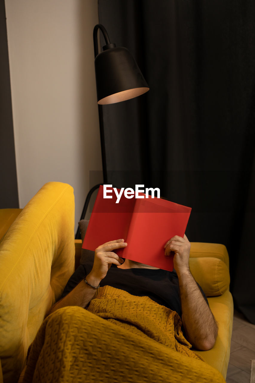 Man reading book while lying on sofa at home