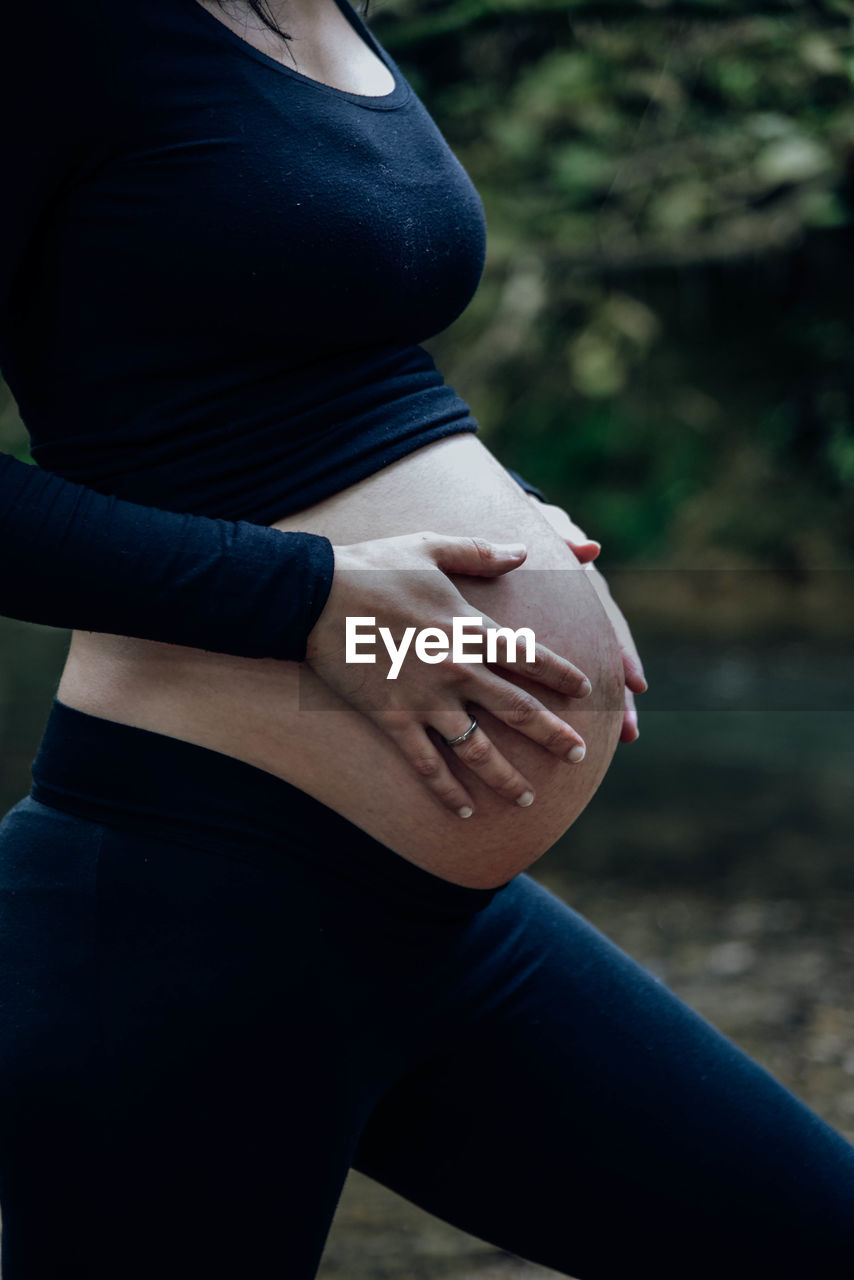 Midsection of pregnant woman touching belly while standing outdoors