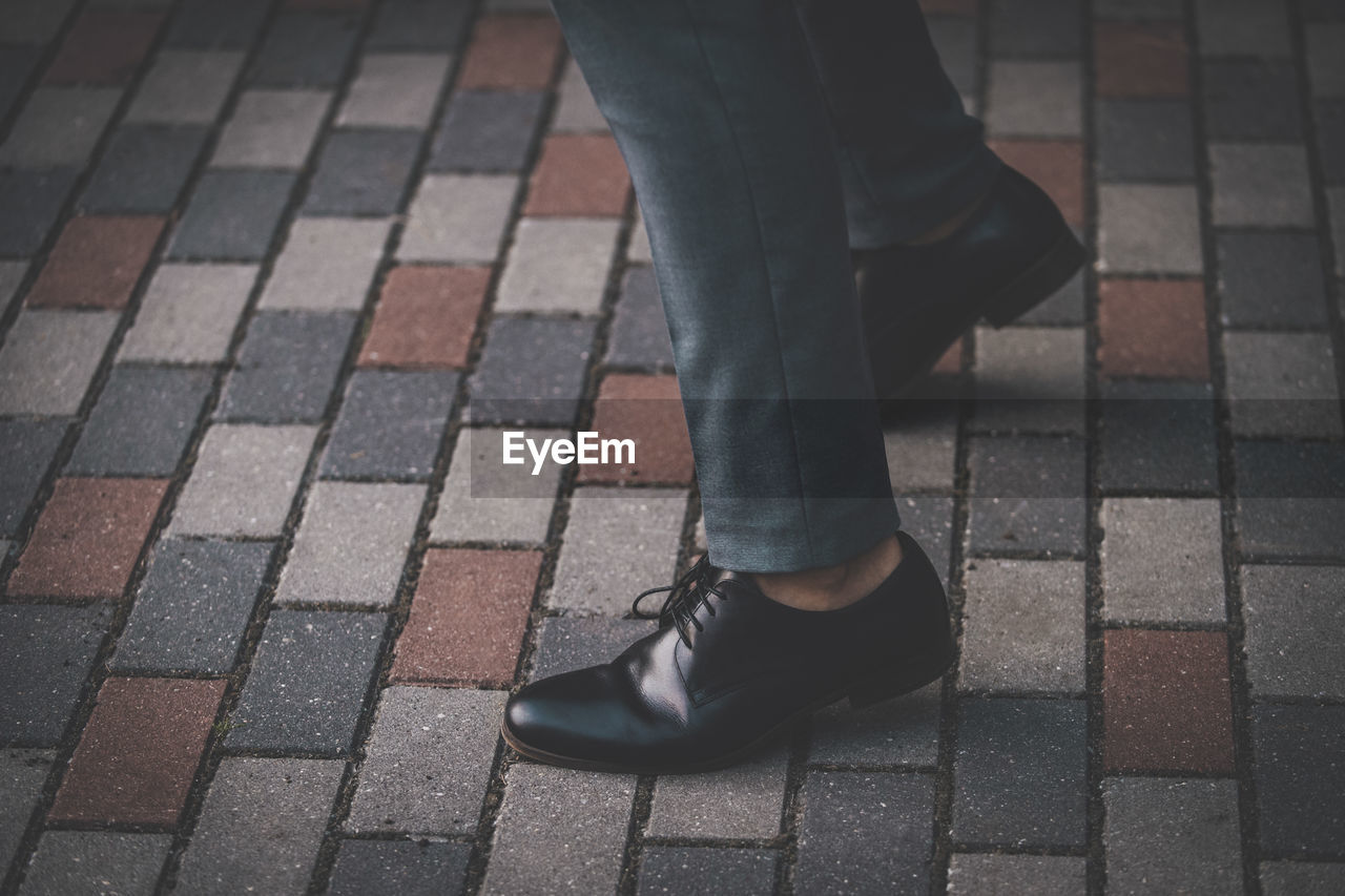 Low section of businessman wearing shoes while standing on footpath