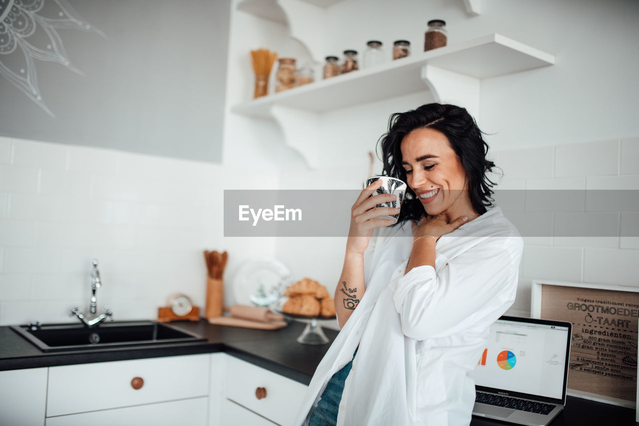 Smiling woman holding coffee cup standing in kitchen