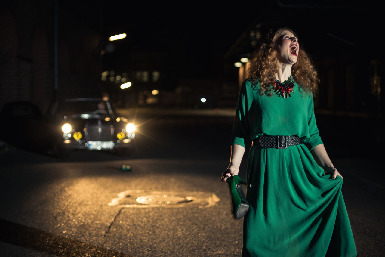 Young woman screaming against vintage car on road during night