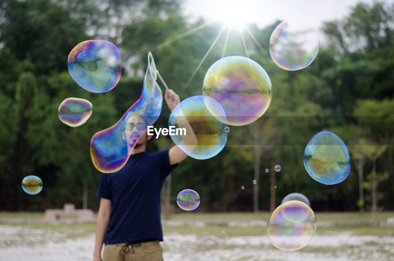 Mature man making bubbles while standing against trees