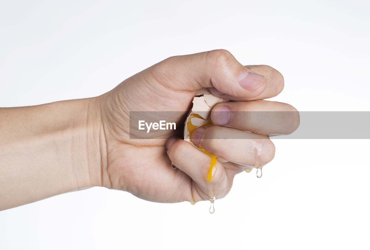 Cropped hand of woman breaking egg over white background