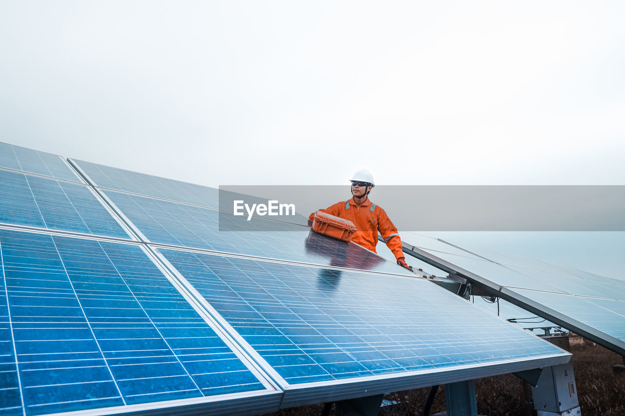 Engineer fixing solar panel against sky