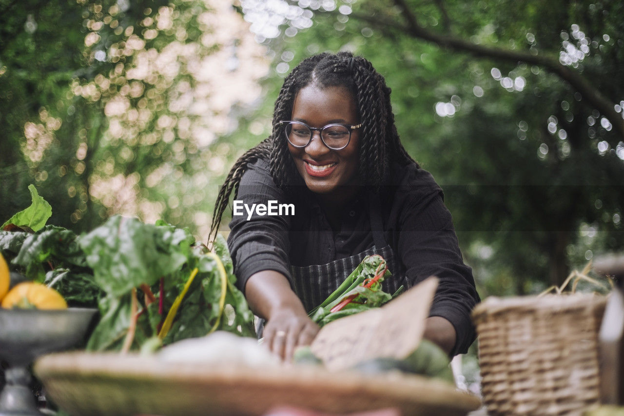 Smiling female vendor with braided hair arranging vegetables at market