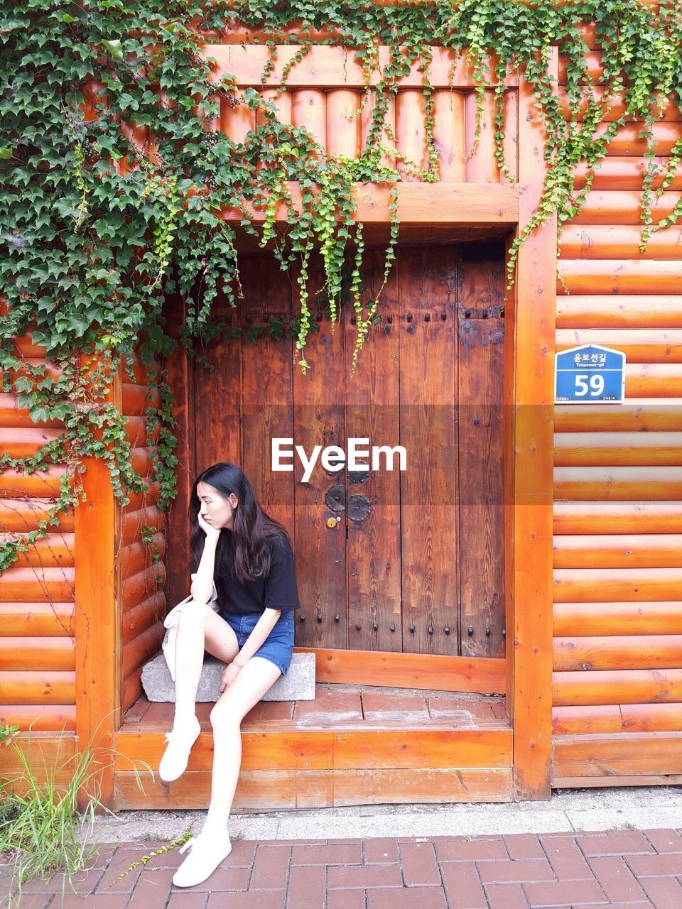 Woman with hand on chin sitting against wooden door