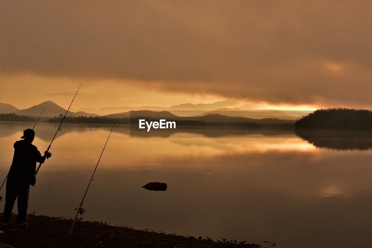 Silhouette man fishing in lake against sky during sunset