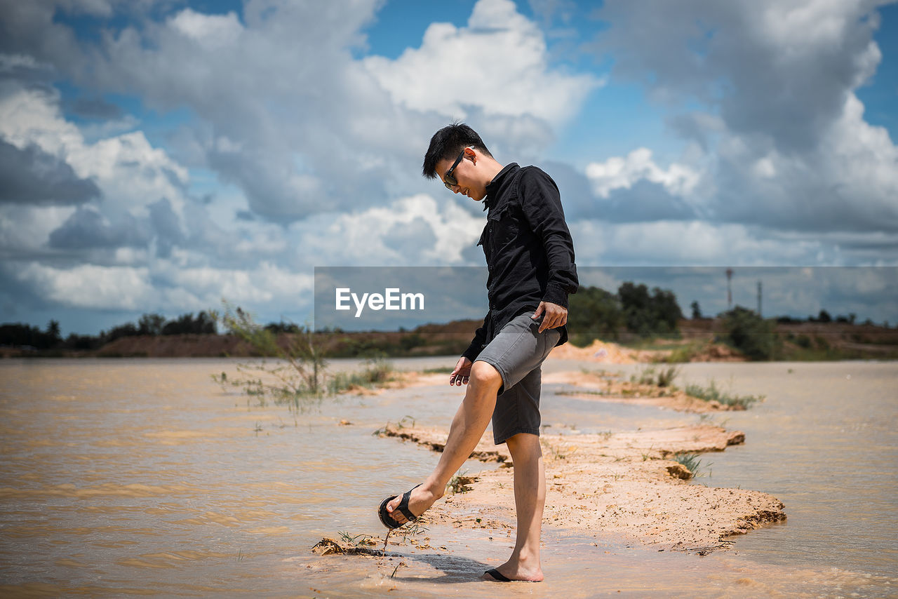 Young man standing at beach against sky